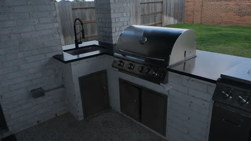 Outdoor sink with black faucet and the grill on the black granite counter