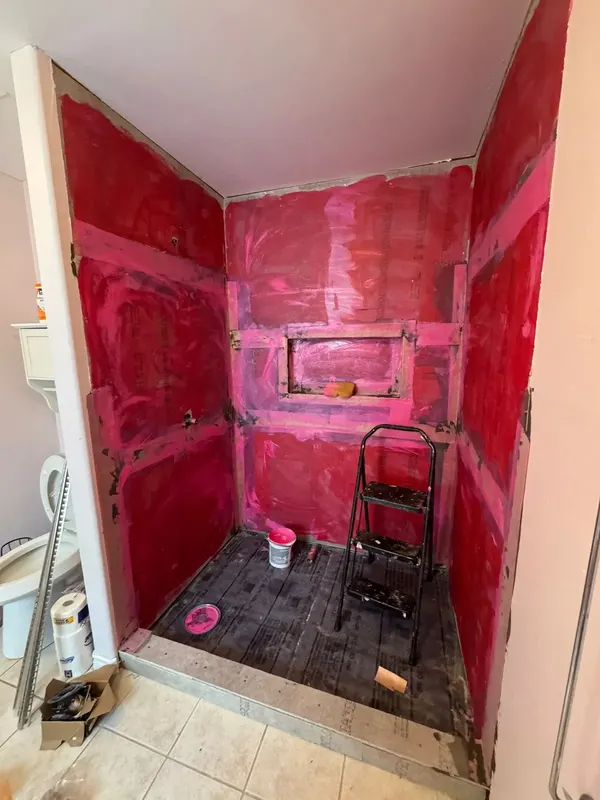 Red liquid waterproofing membrane over the shower walls, niche and bench