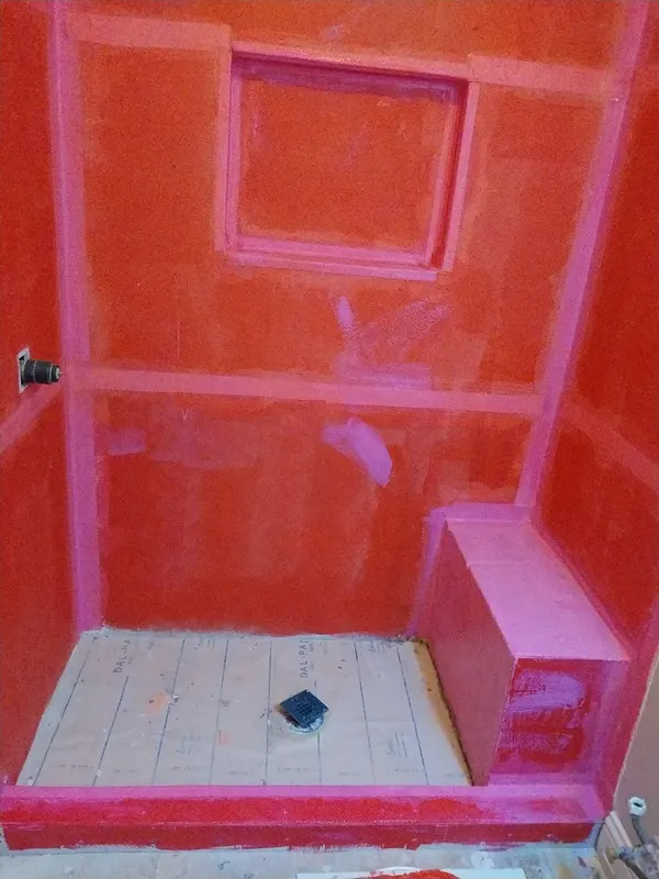Red liquid waterproofing over the shower walls and bench