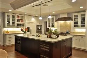 Modern kitchen with white cabinets, a large dark wood island with built-in shelves, pendant lights, stainless steel appliances, and under-cabinet lighting. Flowers and decorative items are arranged on the island countertop.