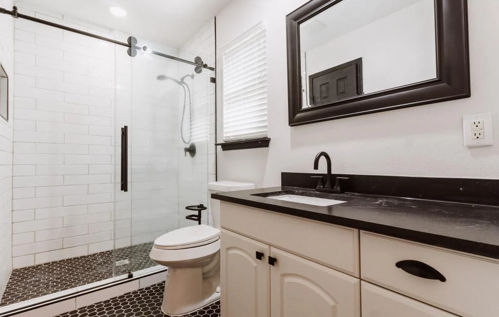 Modern bathroom with a glass-enclosed shower, white subway tile walls, black hexagonal floor tiles, and a sleek vanity—perfect inspiration for bathroom remodeling Houston homeowners will love.