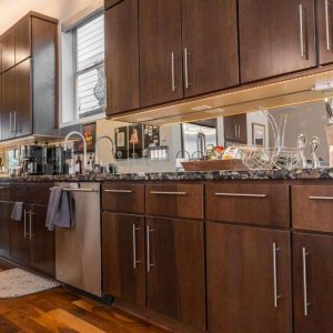Modern kitchen with dark wood cabinets, stainless steel appliances, and a granite countertop. Kitchen items and decor, including utensils, a dish rack, and framed photos, are neatly arranged on the counter.