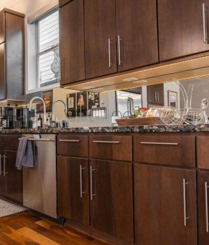 Modern kitchen with dark wood cabinets, stainless steel appliances, and a granite countertop. Kitchen items and decor, including utensils, a dish rack, and framed photos, are neatly arranged on the counter.