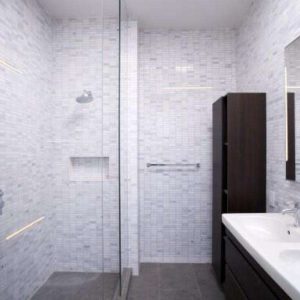 Modern bathroom with white tiled walls, a glass-enclosed shower, wall-mounted showerhead, built-in shower niche, dark wood cabinets, large mirror, and a double sink vanity.